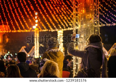 Christmas market and concert in city centre. People enjoying event, taking pictures and videos. Beautiful decorations and glowing lights.  
