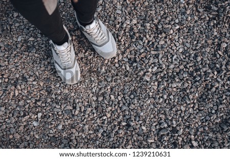Women's gray sport sneakers stand on gravel in the evening light. Top view.