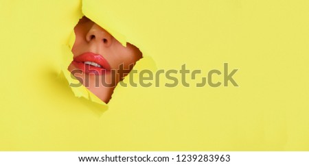 View of bright lips through hole in yellow paper background. Make up artist, beauty concept. Cosmetics sale. Beauty salon advertising banner with copy space.