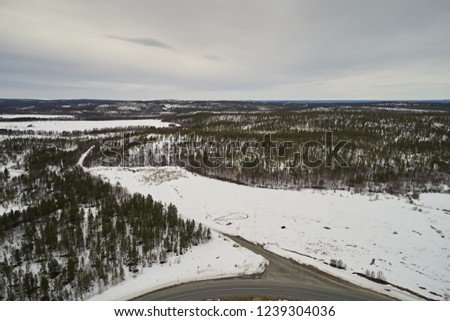 Aerial view of the road and taiga forest in winter on a cloudy day. Abstract landscape of northern nature with drone. 