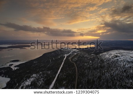 Aerial view of the two road and taiga forest in winter against the bright sunset sky. Beautiful landscape of northern nature with drone. 
