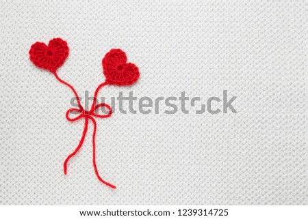Two red crochet wool hearts and ribbon on white crochet background, love story. The concept for 14 February, romantic Valentine day. Festive overhead photo with place for text, copyspace. Love affair