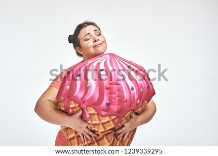 Funny picture of amusing, brunette, chubby woman on white background. Woman is holding a huge ice cream