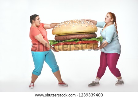 Funny picture of amusing, chubby women on white background. Two women are holding a huge sandwich