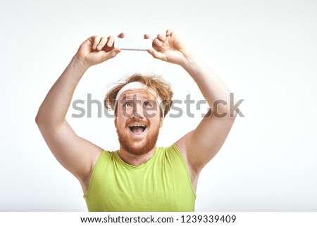Funny picture of red haired, bearded, plump man on white background. Man wearing sportswear. Man smiling and taking a selfie