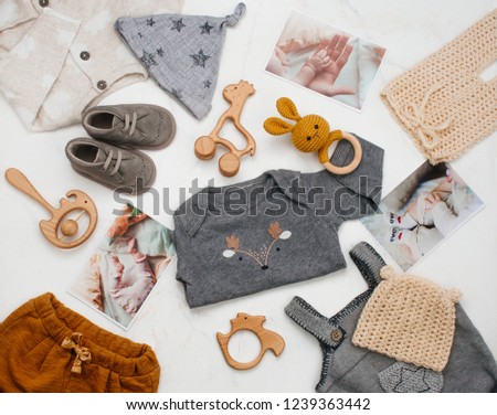 Baby shower concept. Newborn baby clothing, wooden toys and baby photos on white marble background. Top view, flat lay.
