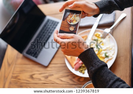 Blogger takes pictures of the Breakfast on the smartphone. Concept of creating content for social networks. Focus on the phone screen. Laptop and eat on the table.. American style breakfast.