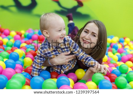 portrait a smiling boy plays in playing centre with mother.
funny boy in pool with multicolored balls.
mom and son have fun together in playroom close up.
conceot of happy childhood.
family weekend.