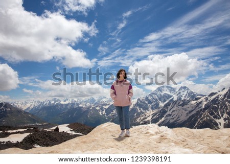 Cute teen girl in a pink jacket blue jeans and white sneakers standing on top of the mountains