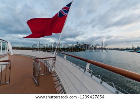 View of New York city skyline and upper Hudson river in morning from deck of a cruise ship docked at Brooklyn Cruise Terminal with red ensign flag in foreground
