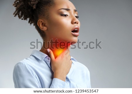 Throat pain. Woman holding her inflamed throat. Photo of african american woman in blue shirt on gray background. Medical concept Royalty-Free Stock Photo #1239453547