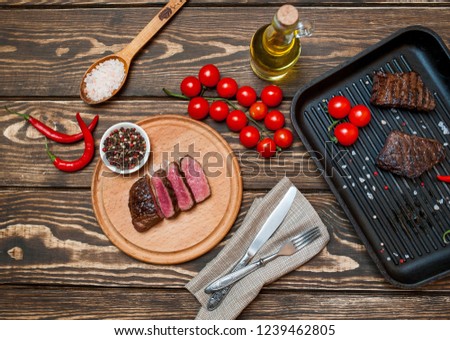 steaks, roast beef in a frying pan with spices, tomatoes, chili pepper, on wooden background, top view, beside chopped beef on a board