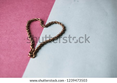 Texture of a beautiful golden festive chain unique weaving in the shape of a heart on a pink purple blue background and copy space. Concept: love, marriage proposal, marriage, St. Valentine's Day.