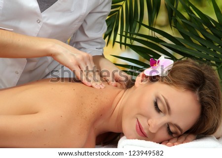 beautiful woman in spa salon  getting massage, on palm leaves background