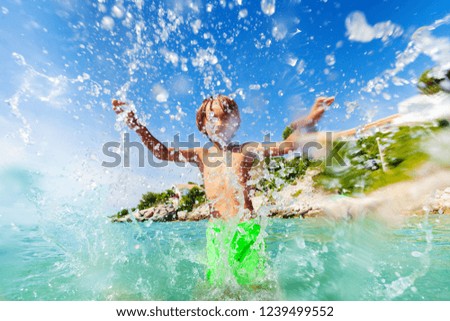 Excited boy having fun splashing water in the sea