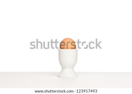 One egg in a egg cup pictured on a table against a white background.