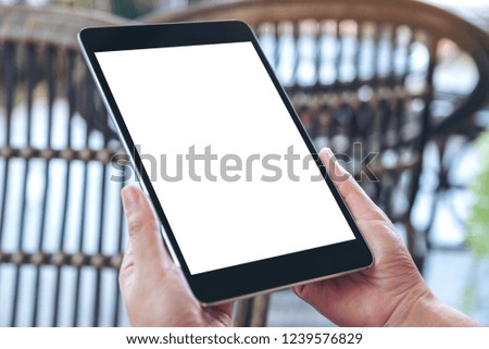 Mockup image of hands holding and using black tablet pc with blank white desktop screen while sitting in the outdoors