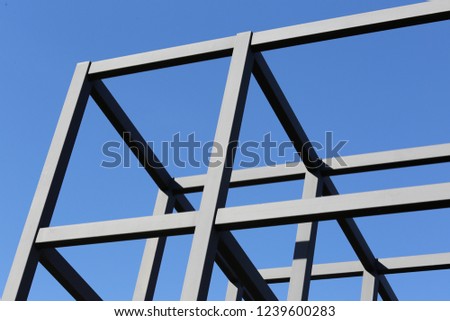 Abstract outdoor view of group of steel assembled beams. Abstract design with iron lines skeleton. Blue vivid sky in background. Framework of a modern building structure. Geometric and graphic shapes.