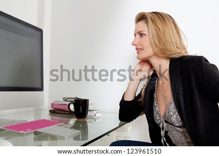 Profile view of an attractive professional woman working at her home office desk, using a desktop computer.