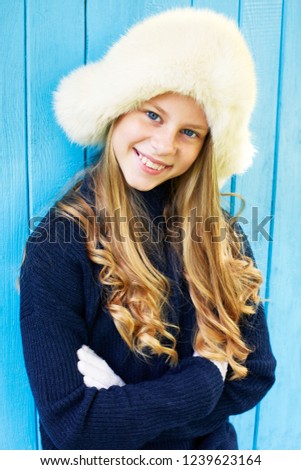 Cheerful little girl in warm sweater. Blue wooden background. 