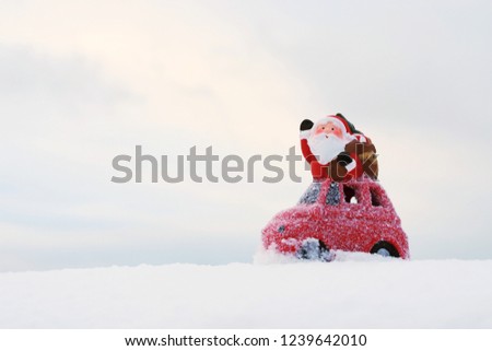 Christmas and New Year background with copy space. Cute Santa Claus with gift bag on a red car among real white snow  against gray-blue sky