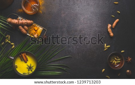 Golden turmeric milk with spices. Dark background frame with ingredients and palm leaves. Healthy hot drink. Immune boosting remedy , detox and dieting concept Royalty-Free Stock Photo #1239713203