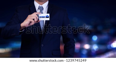 Property insurance and security concept. Real estate agent man hold business card on city night background.