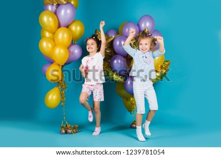 Happy little girl sisters in pajamas dance with balloons on a blue background