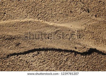 Close up outdoor view from above of a sandy eroded soil with water traces. Wet surface with flow shapes. Symbolic image of erosion of land due to the rainfalls. Natural picture of a brown ground.