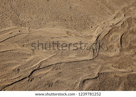 Close up outdoor view from above of a sandy eroded soil with water traces. Wet surface with flow shapes. Symbolic image of erosion of land due to the rainfalls. Natural picture of a brown ground.