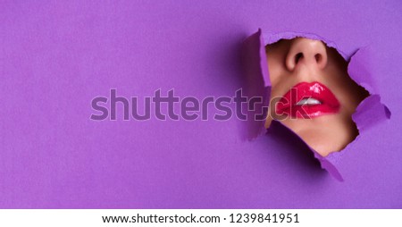 View of bright lips through hole in violet paper background. Make up artist, beauty concept. Cosmetics sale. Beauty salon advertising banner with copy space.