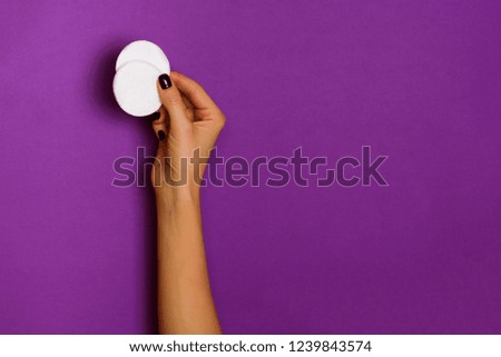 Female hands holding white cotton pad on violet background. Banner. Skin care, pure beauty, body treatment concept.