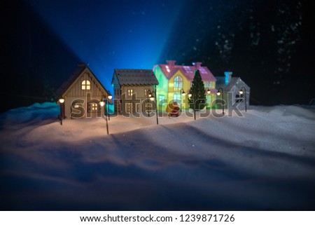 Little decorative cute small houses in snow at night in winter, Christmas and New Year miniature house in the snow at night with fir tree. Holiday concept . Selective focus