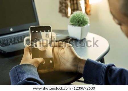 man using smart phone to take picture of tea cup and laptop computer on the table.