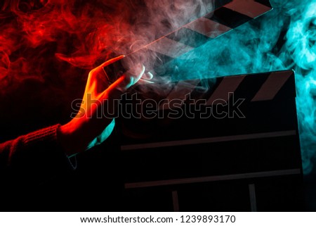Close-up on an open clapper in hand before starting shooting a film with multi-colored smoke around with red and green backlighting on a black isolated background