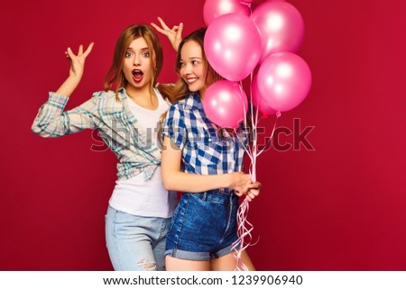 Two smiling beautiful women in checkered shirt clothes.Girls posing on red background.Models with pink balloons.Having fun,ready for celebration birthday or holiday party