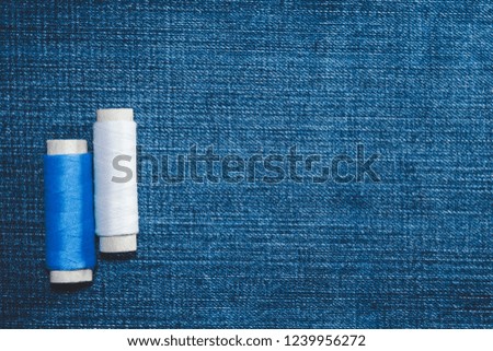 Spools of white and blue cotton thread on jeans fabric with copy space