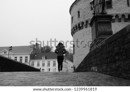 Woman walks across historic bridge to the broel towers in kortrijk.
