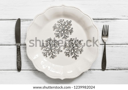 Christmas table setting ,silver snowflakes on a white plate, vintage cutlery, fork and knife. White wooden wooden table. Top view, flat lay