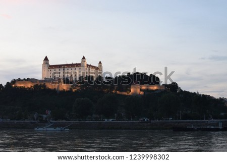 Bratislava castle at dusk during sunset, massive rectangular building with four corner towers stands on an isolated rocky hill of the Little Carpathians directly above the Danube river