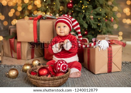 The little girl under the Christmas tree. baby girl in Santa Claus hat with gifts under Christmas tree at fireplace with piggy toy