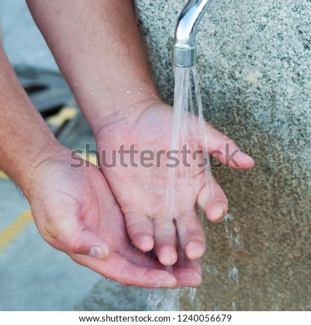 Man washes his hands in a street water tap (square format of picture)