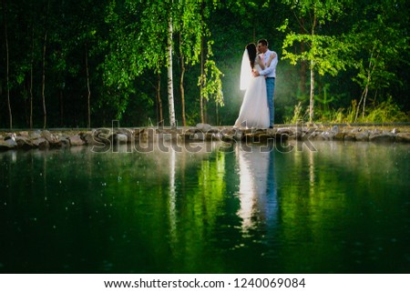 Newlywed couple standing next to a pond in the rain and hugging