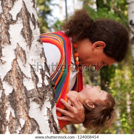 Happy father and baby playing and laughing in birch forest. Baby sitting in a sling.