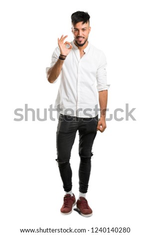 A full-length shot of a Arabic young man with white shirt showing an ok sign with fingers on isolated white background