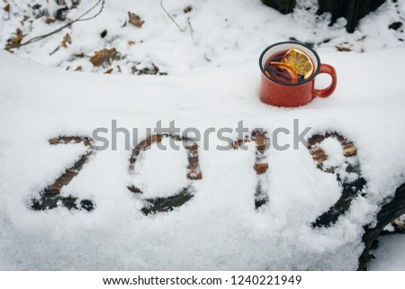 The number 2019 in the snow with a cup of mulled wine in the winter snowy forest. New Year's eve concept. Christmas background with snowflakes