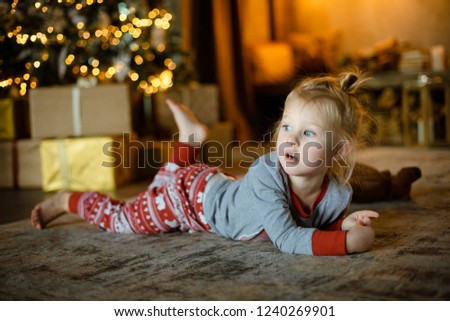 Charming little blonde on the carpet on the background of a decorated Christmas tree and burning garlands. Cozy Christmas concept