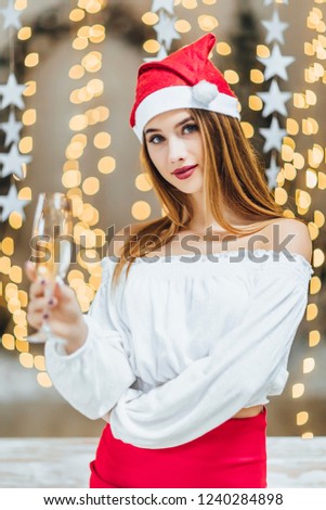 A young beautiful girl in a Santa Clause hat, holding a glass of champagne and a bottle of her on a New Year's photo shoot in the studio. The New Year Concept.