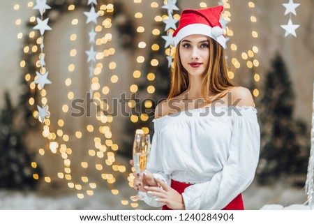 A young beautiful girl in a Santa Clause hat, holding a glass of champagne and a bottle of her on a New Year's photo shoot in the studio. The New Year Concept.