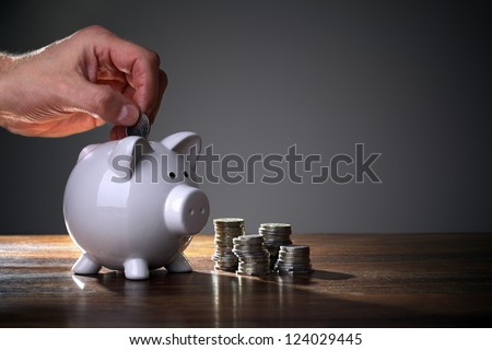 Inserting a coin into a piggy bank Royalty-Free Stock Photo #124029445